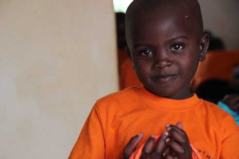 A young Rwandan boy in an orange T-shirt.